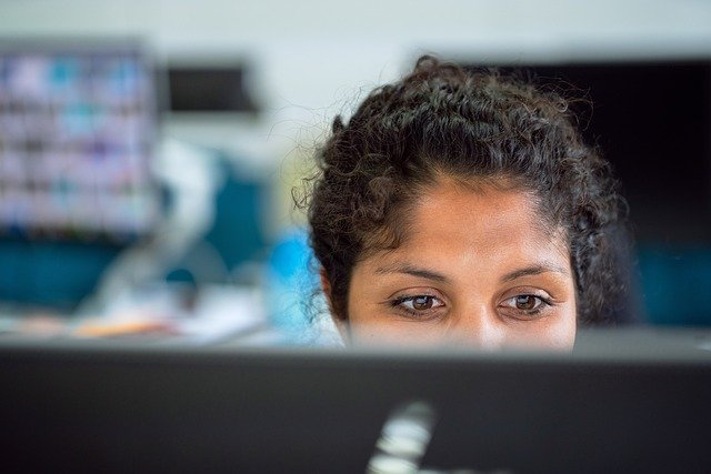 Top half of a woman's face appears from behind the laptop screen of cybersecurity careers she is looking at